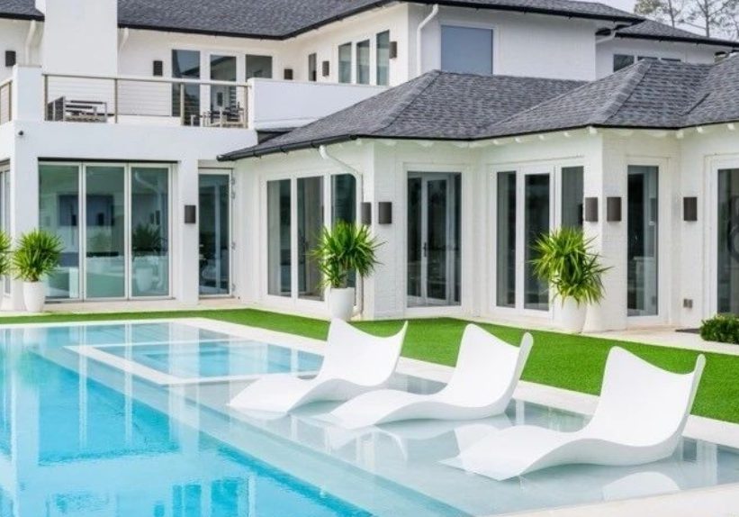A pool with white chairs and grass around it.